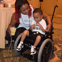a small child smiling in his wheelchair with his mother.